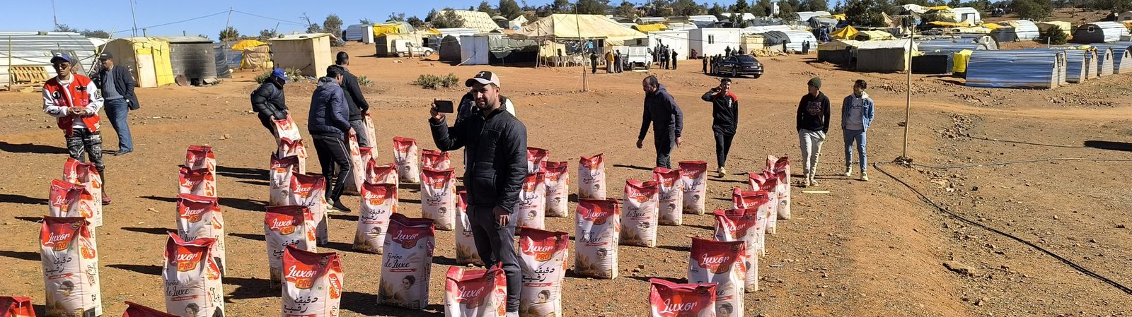 Aid laid out in rows on the ground at a High Atlas distribution, volunteers and vehicles behind