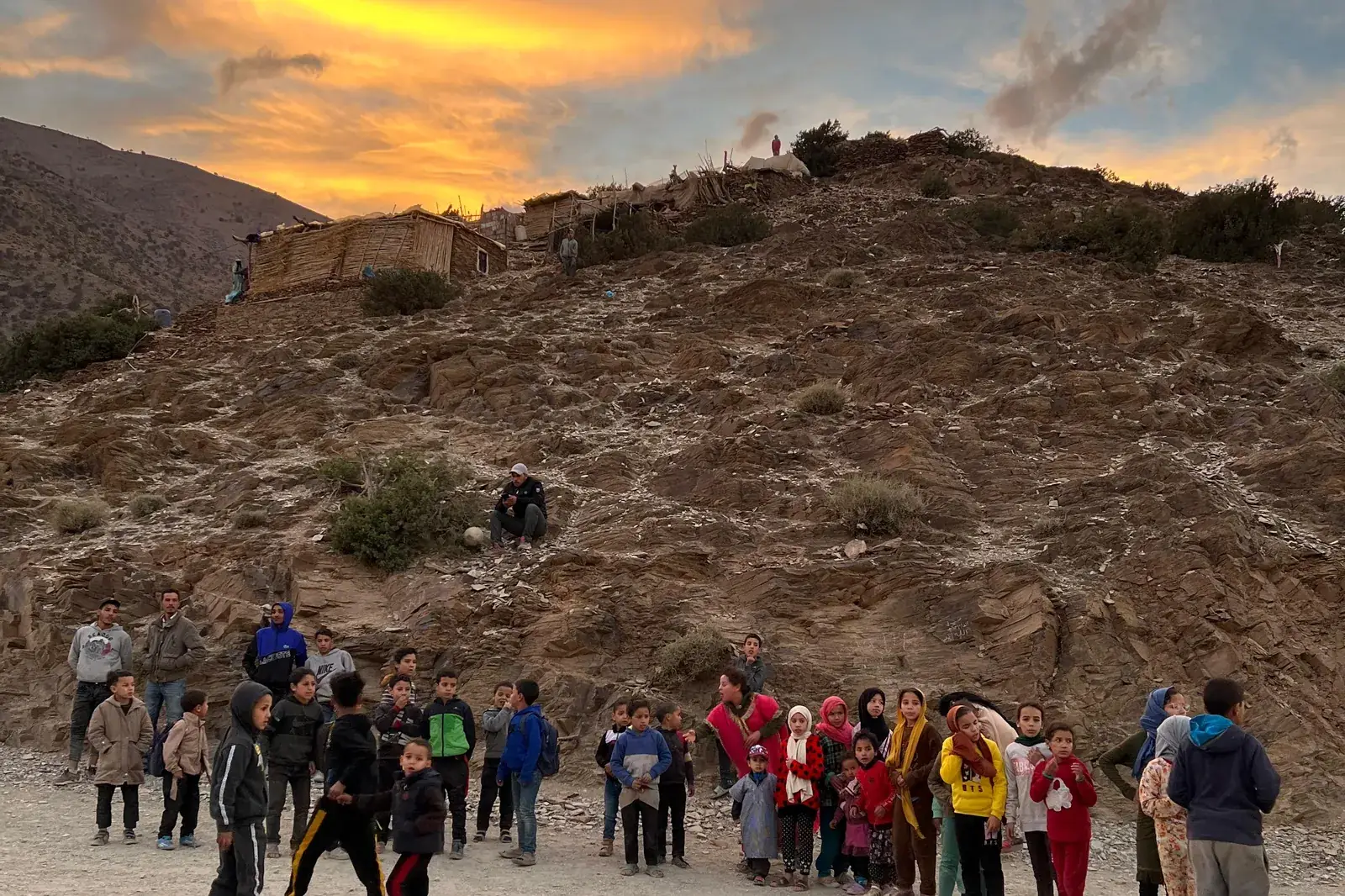 Village children gathered on a mountain track at sunset below the High Atlas Mountains