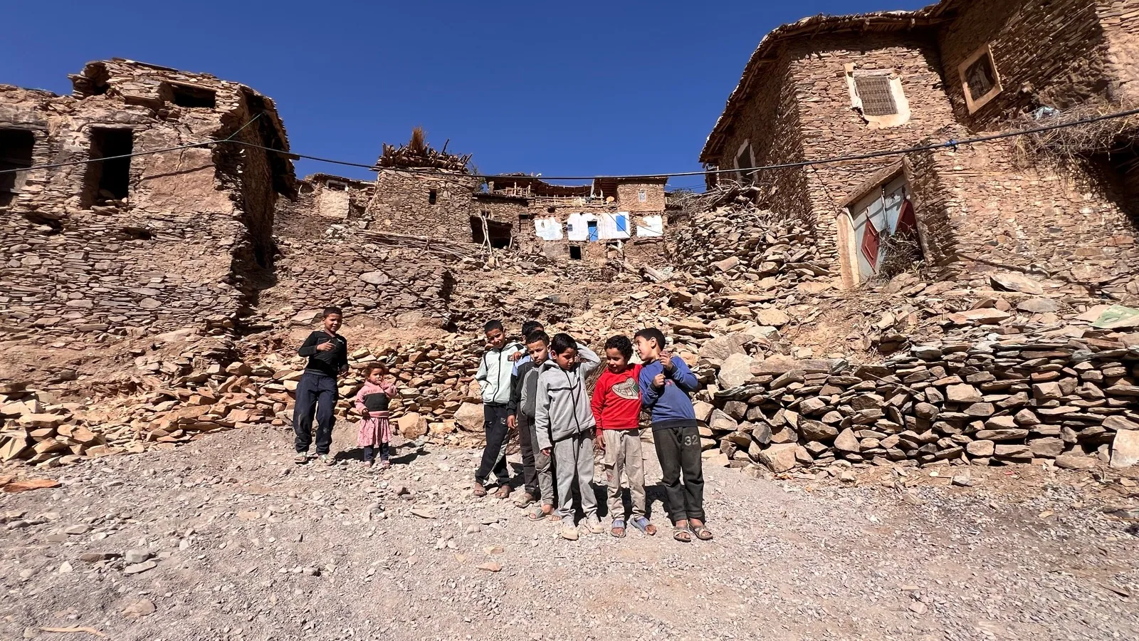 Children stand below earthquake-damaged stone homes in Ijoukak in the High Atlas Mountains