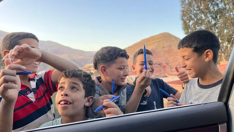 Three boys examining new pens and stationery with mountains behind