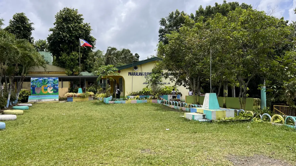 The grassy grounds of Cabalabaguan Elementary School with classrooms, shade trees and the Philippine flag
