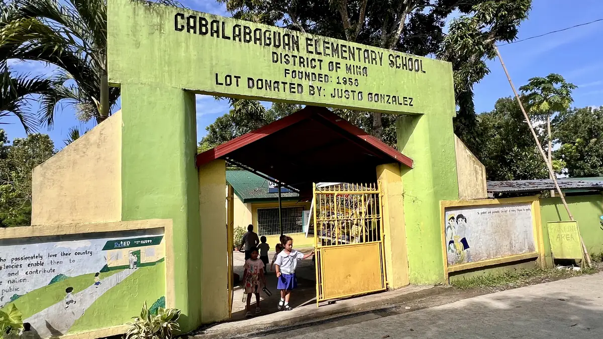 Green entrance arch of Cabalabaguan Elementary School, District of Mina, founded 1958, with pupils walking through the gate