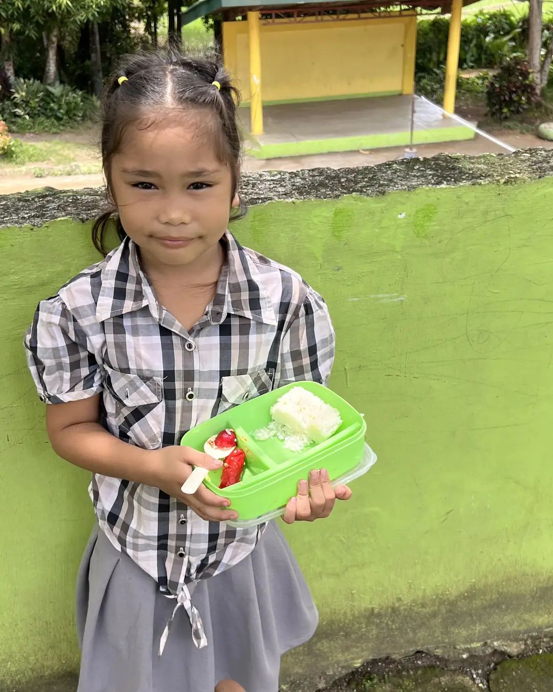 A young pupil at Cabalabaguan Elementary School smiling and holding an open green lunch box
