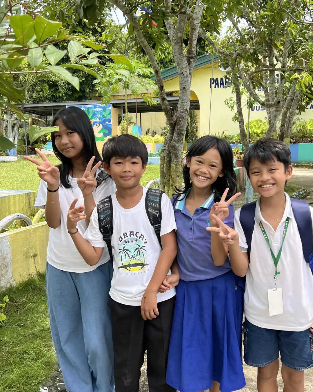 Four pupils of Cabalabaguan Elementary School smiling and making peace signs on the school grounds